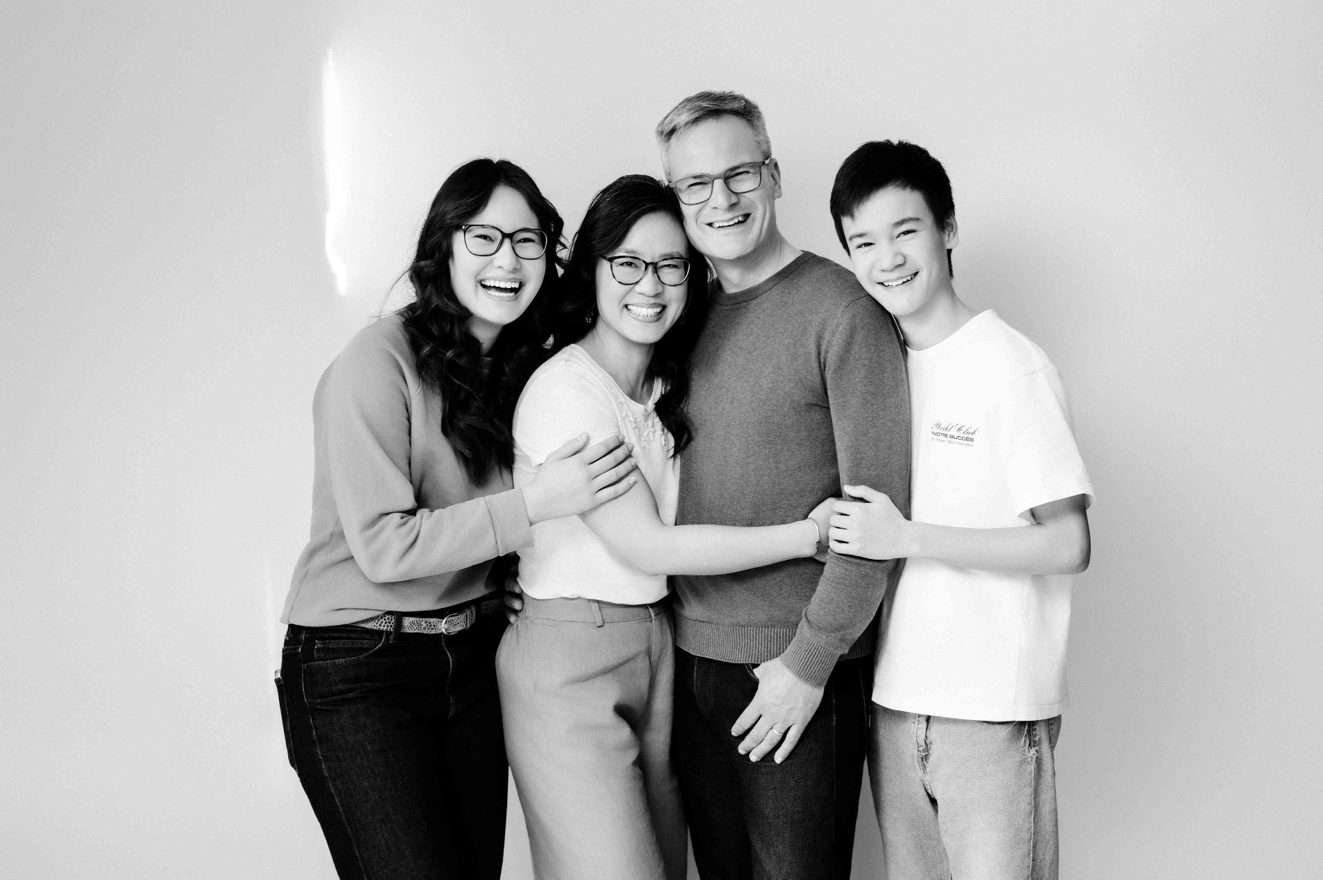 A family of four standing close together, all smiling in soft black and white.