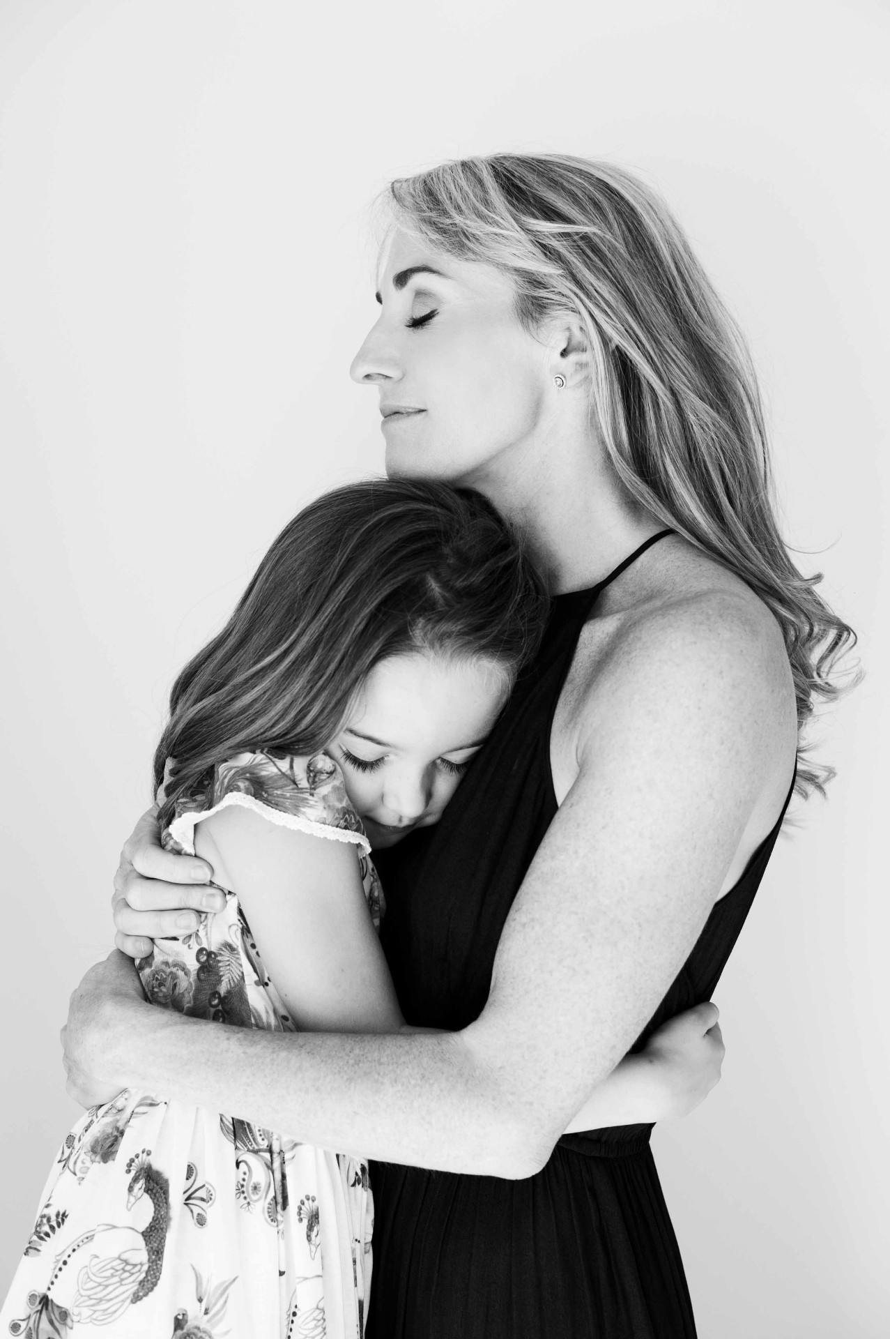A mother holding her daughter close, eyes gently closed.