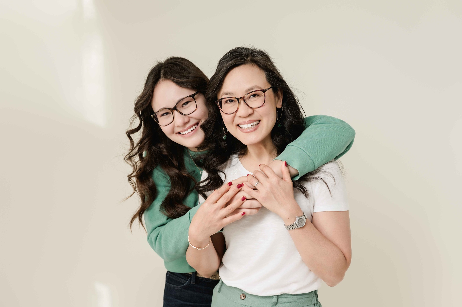 A teenage daughter hugging her mother from behind, both beaming.