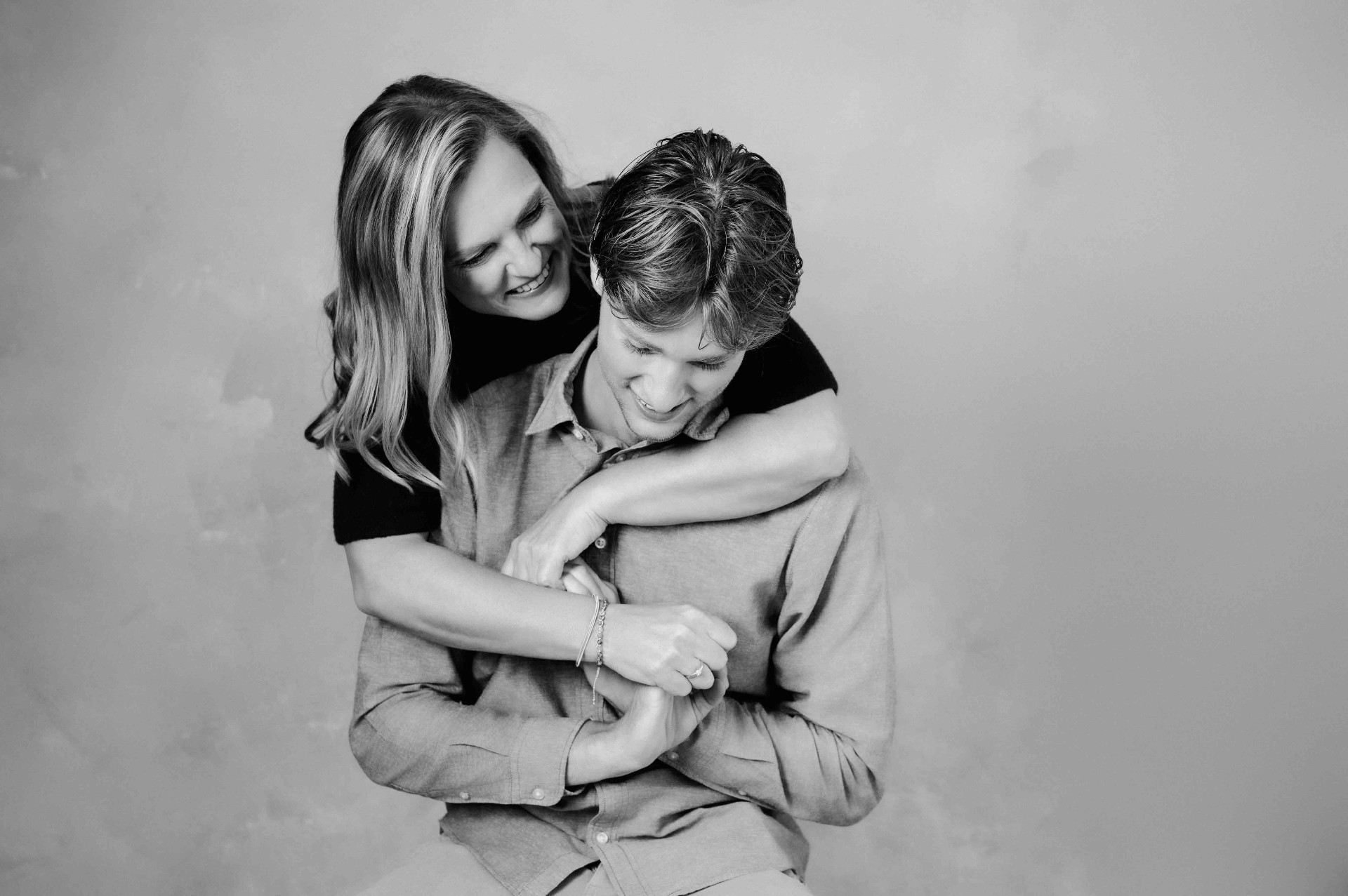 A mother hugging her grown son from behind, both smiling softly.