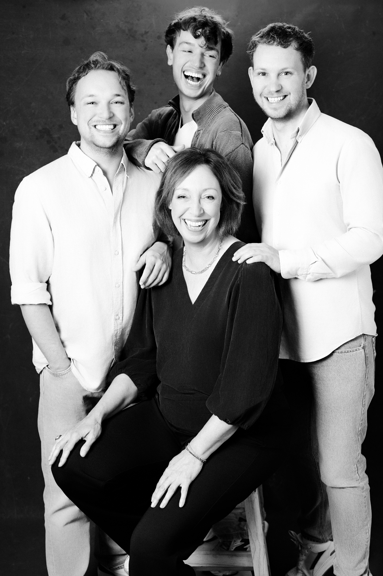 A mother seated with her three grown sons, all laughing together.