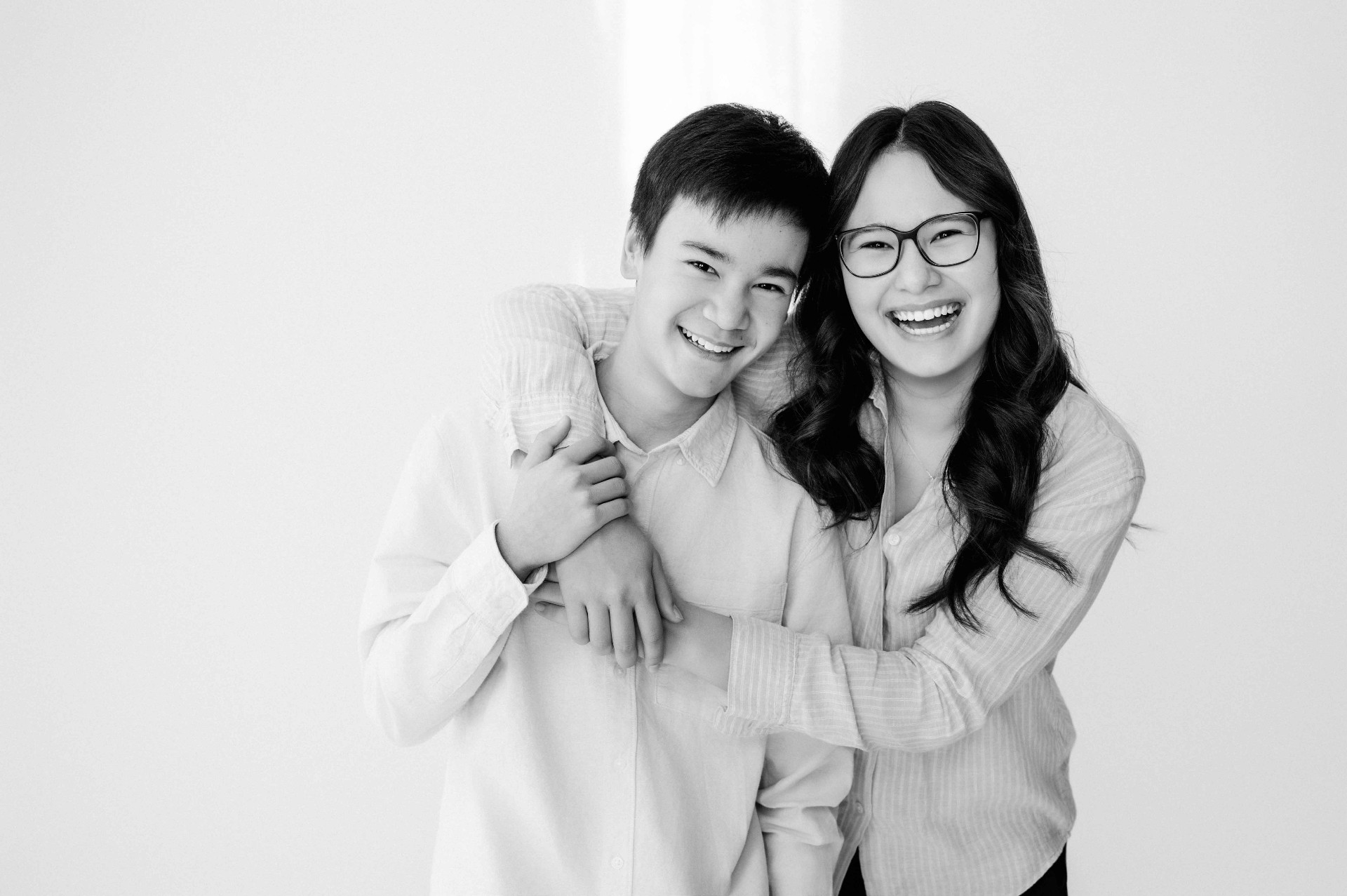 A brother and sister leaning in together, laughing.