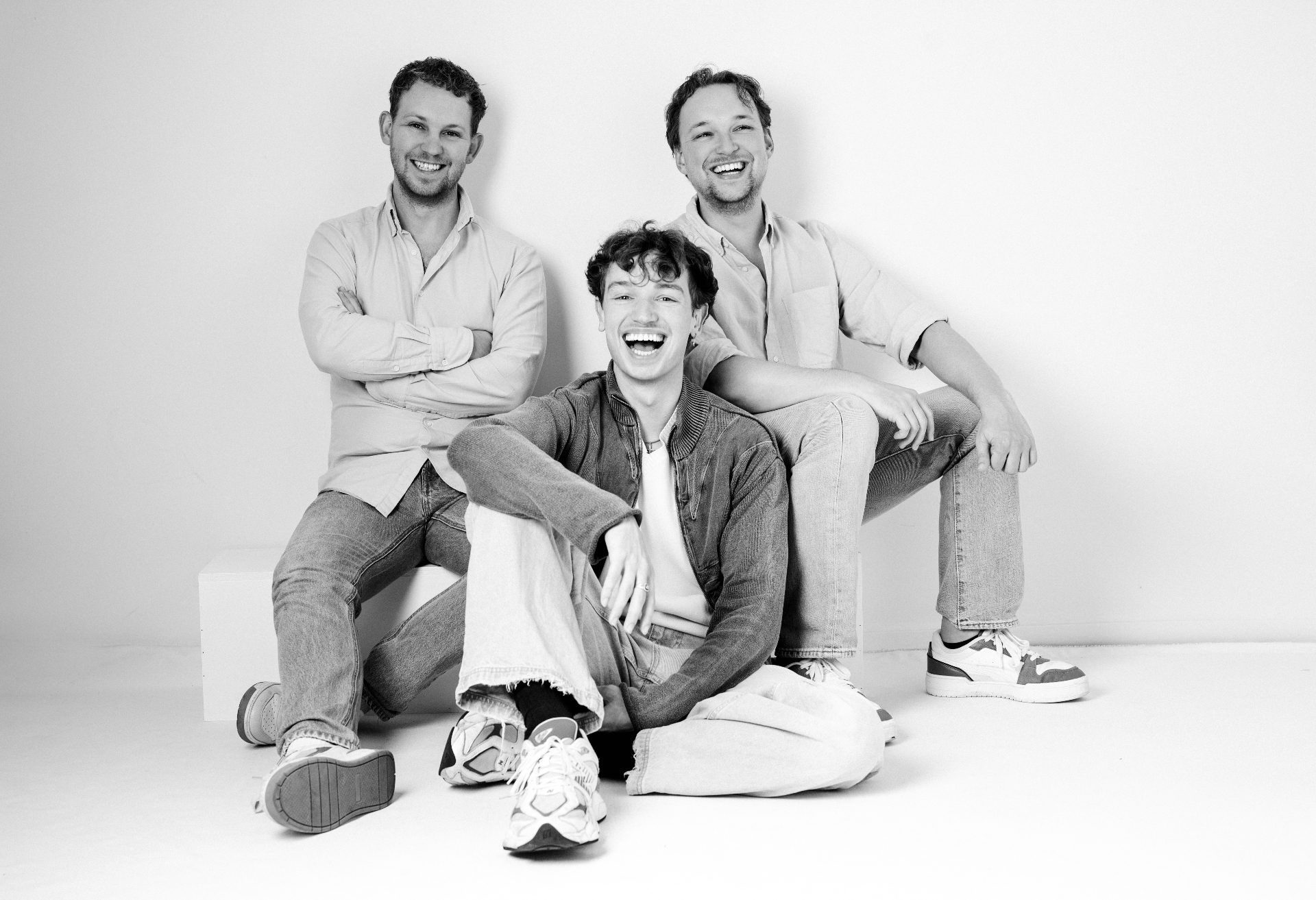 Three brothers relaxed in the studio, mid-laugh.