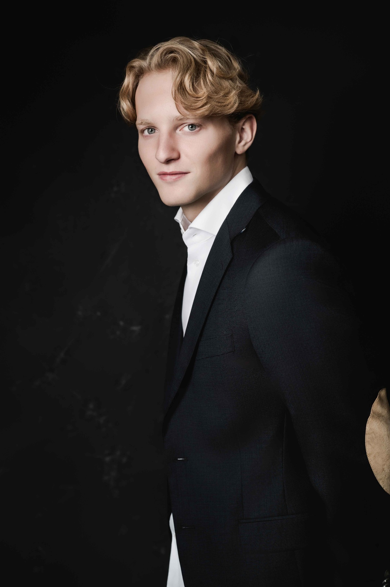 A portrait of a young man in a tailored suit against a dark backdrop.